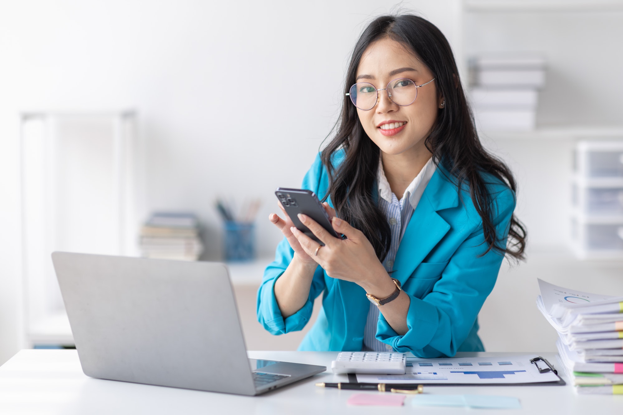 Business Asian woman hold phone and use laptop at the workplace. Project stats financial data sales